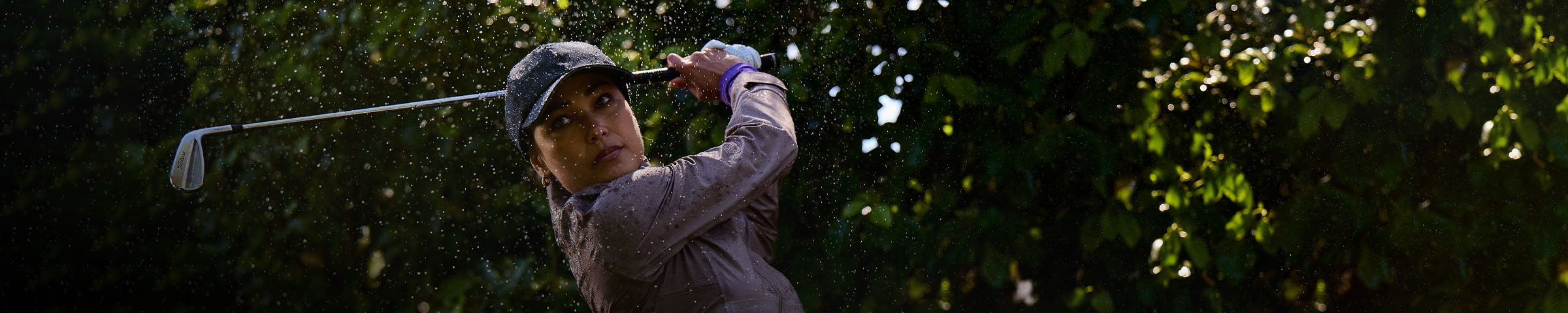 A woman wearing a KJUS Pro 3L 3.0 swings a golf club in the rain.